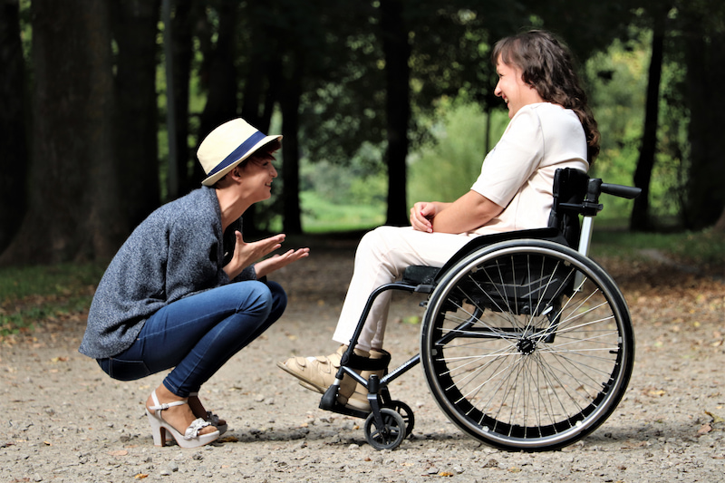 Two people chatting, one on a wheelchair one crouching down