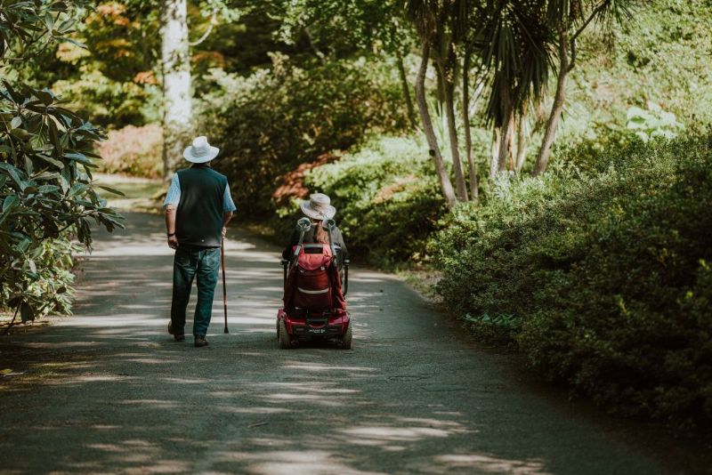 Couple walking in the woods, one on a wheelcair one walking