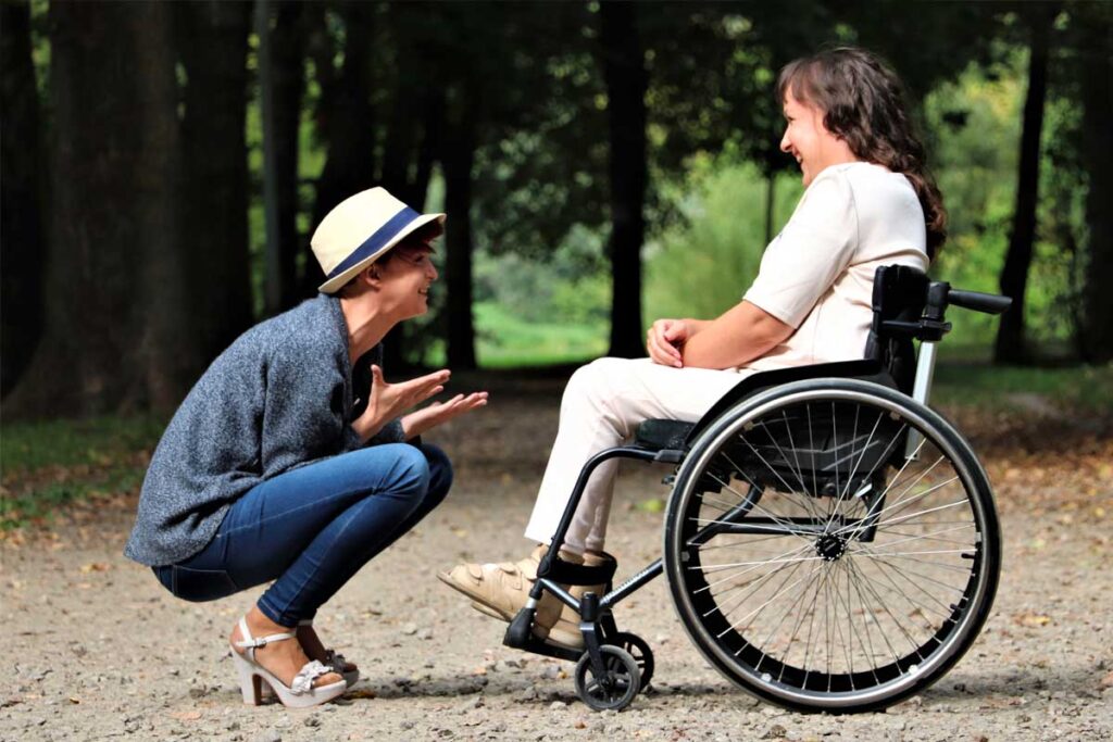 Two people chatting, one on a wheelchair one crouching down